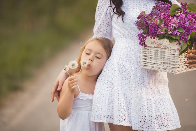 Giovane bella madre e figlia piccola divertirsi insieme. Mamma graziosa e ragazza carina all'aperto. Famiglia allegra insieme. Bambino che soffia su un blowball