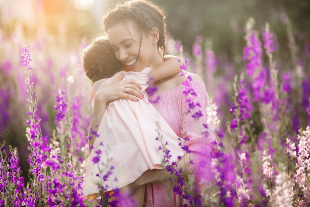 Giovane bella madre e la sua piccola figlia all'aperto con i fiori. Campo di fiori viola