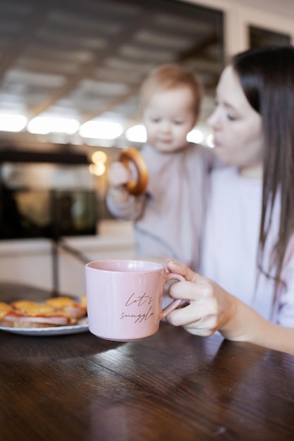 Giovane bella mamma blogger che beve caffè alla sua scrivania e tiene in braccio un bambino