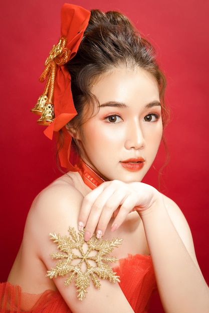 Giovane bella modella asiatica in un elegante vestito rosso di lusso su uno sfondo rosso isolato