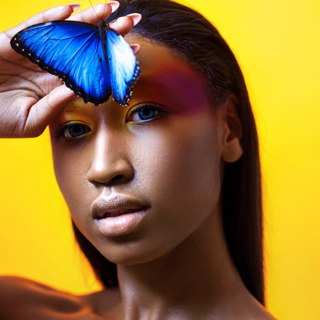 Giovane bella ragazza afro, con farfalla blu, ritratto di bellezza