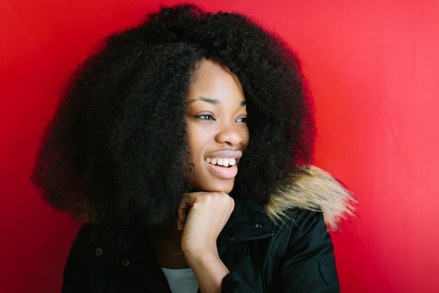 Giovane bella ragazza afroamericana in un cappotto nero che sorride sul fondo rosso