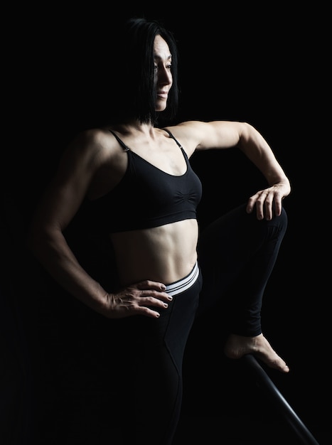 Giovane bella ragazza atletica con i muscoli in uniforme nera in posa lateralmente