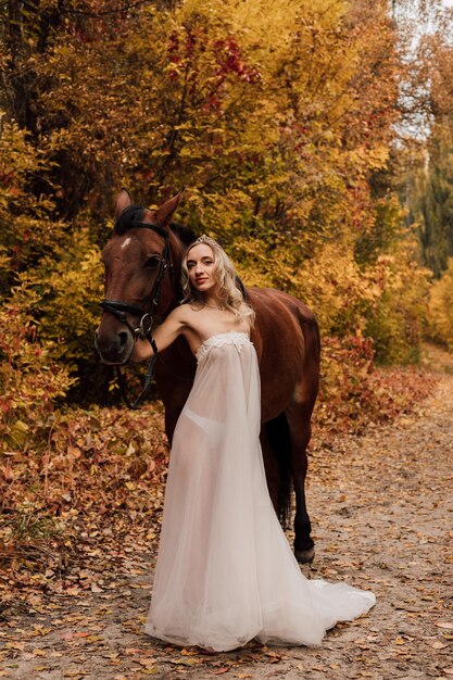 Giovane bella ragazza bionda in posa in un parco autunnale con un cavallo