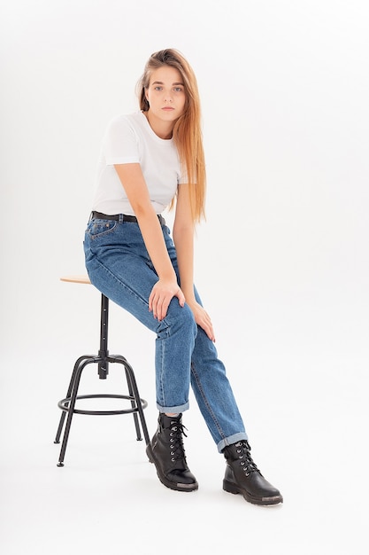 Giovane bella ragazza caucasica con i capelli lunghi in maglietta, jeans blu allo studio