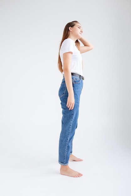 Giovane bella ragazza caucasica con i capelli lunghi in maglietta, jeans blu allo studio