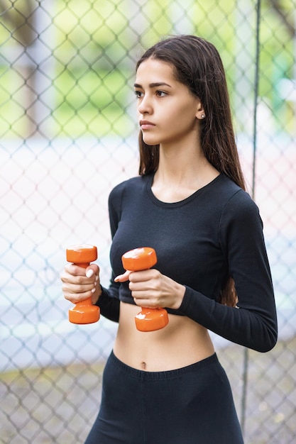 Giovane bella ragazza che conduce un allenamento di stile di vita sano in abbigliamento sportivo per strada con manubri