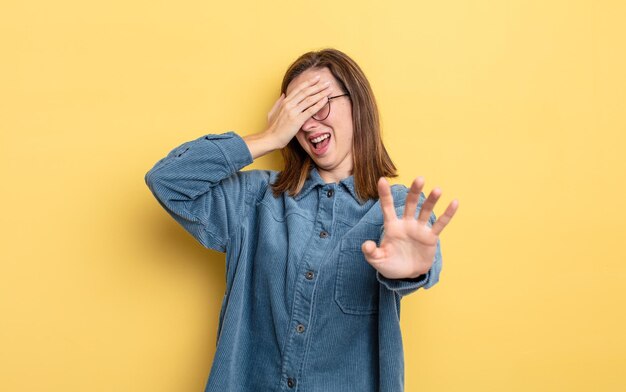 Giovane bella ragazza che copre il viso con la mano e mette l'altra mano davanti per impedire alla fotocamera di rifiutare foto o immagini