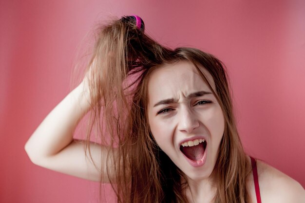 Giovane bella ragazza che ha problemi mentre capelli su sfondo rosa