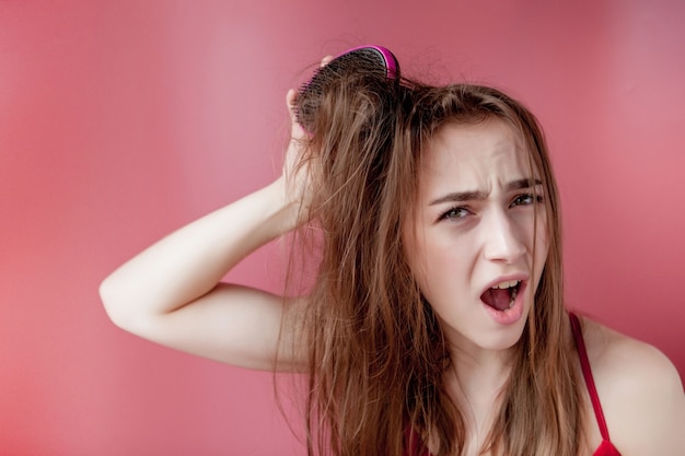 Giovane bella ragazza che ha problemi mentre capelli su sfondo rosa