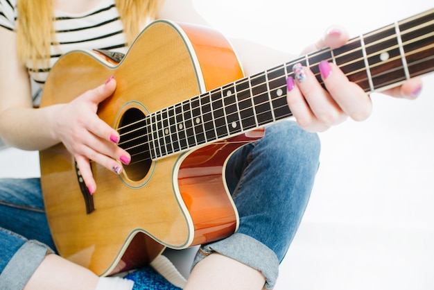 Giovane bella ragazza che indossa jeans e una maglietta a righe con una chitarra acustica su sfondo bianco