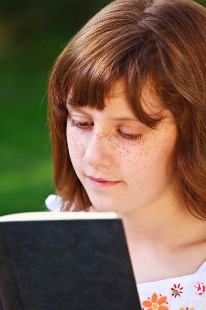 Giovane bella ragazza che legge un libro all'aperto