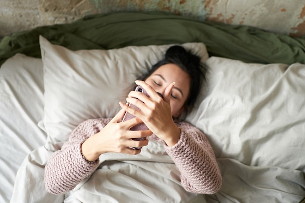 Giovane bella ragazza che manda un sms sullo smartphone mentre giaceva a letto a casa