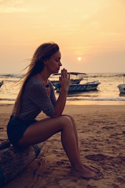 Giovane bella ragazza che prega in riva all'oceano