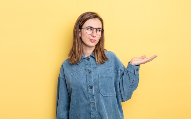 Giovane bella ragazza che si sente felice e sorride casualmente, guardando un oggetto o un concetto tenuto per mano sul lato