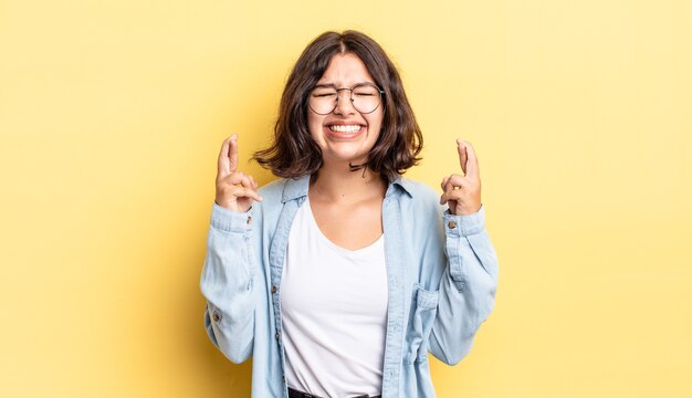 Giovane bella ragazza che si sente nervosa e piena di speranza, incrociando le dita, pregando e sperando in buona fortuna