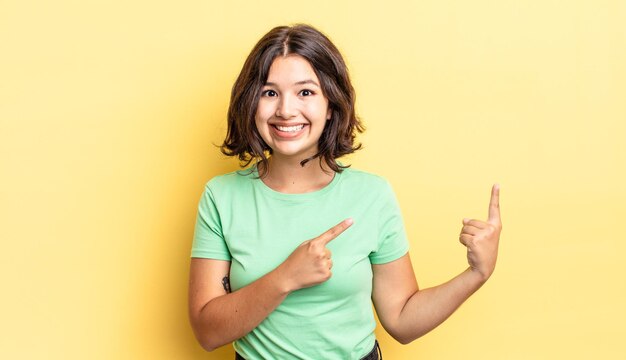 Giovane bella ragazza che sorride felicemente e indica il lato e verso l'alto con entrambe le mani che mostrano l'oggetto nello spazio della copia