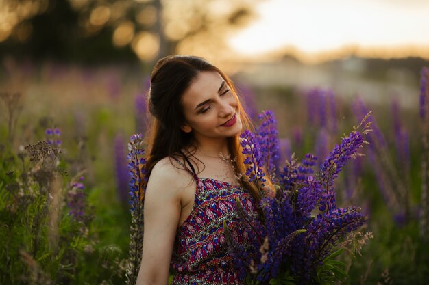 Giovane bella ragazza che tiene un grande fiore con lupino viola in un campo di fioritura. Fiori di lupino in fiore.