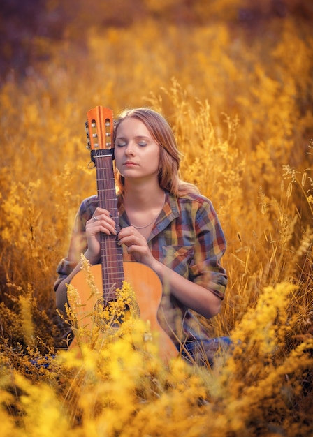 Giovane bella ragazza con gli occhi chiusi si siede in un campo in una chitarra acustica