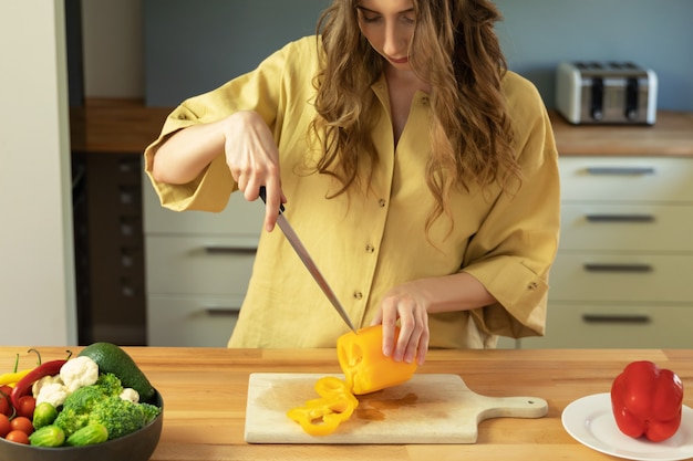 Giovane bella ragazza con i capelli lunghi affetta il peperone dolce. Una donna prepara un'insalata di verdure fresche e sane.