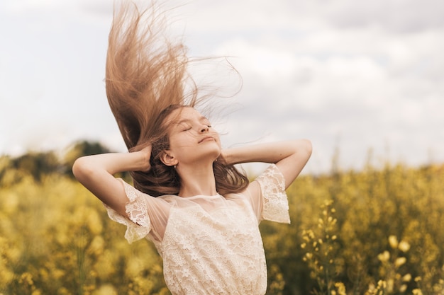 Giovane bella ragazza con i capelli lunghi che volano nel vento sullo sfondo del campo di colza. Brezza che gioca con i capelli della ragazza