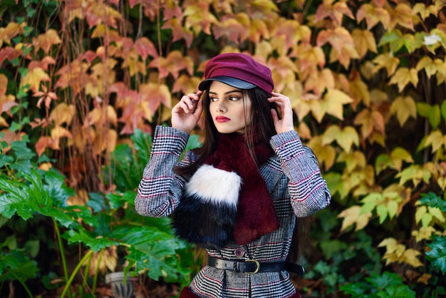 Giovane bella ragazza con i capelli molto lunghi che indossa cappotto e berretto invernale in autunno foglie