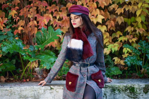 Giovane bella ragazza con i capelli molto lunghi che indossa cappotto e berretto invernale in autunno foglie