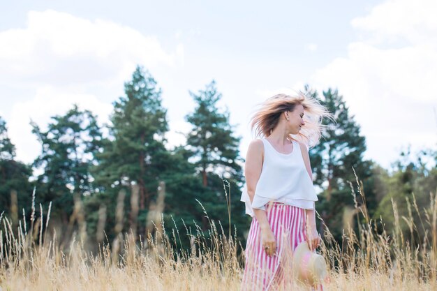 Giovane bella ragazza con i capelli rosa con il cappello estivo che cammina nel campo dorato