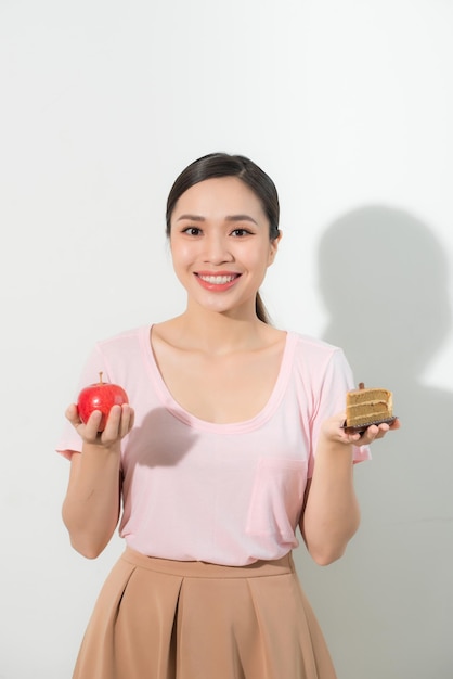 Giovane bella ragazza con mela e torta in mano su uno sfondo bianco. Concetto di cibo sano