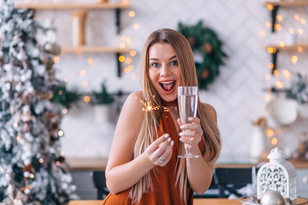 Giovane bella ragazza dai capelli lunghi che tiene un bicchiere di champagne e una stella filante per le vacanze di Natale