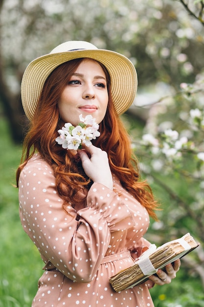 Giovane bella ragazza dai capelli rossi cammina in un frutteto di mele in fiore primaverile