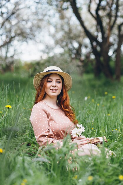 Giovane bella ragazza dai capelli rossi cammina in un frutteto di mele in fiore primaverile