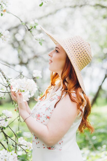 Giovane bella ragazza dai capelli rossi cammina in un frutteto di mele in fiore primaverile