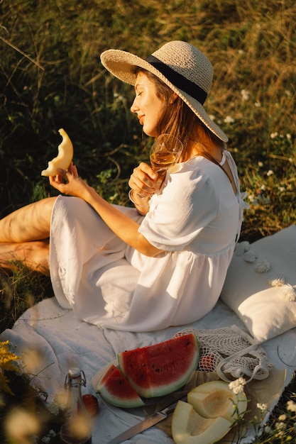 Giovane bella ragazza in abito bianco che fa un picnic con un bicchiere di champagne o vino bianco