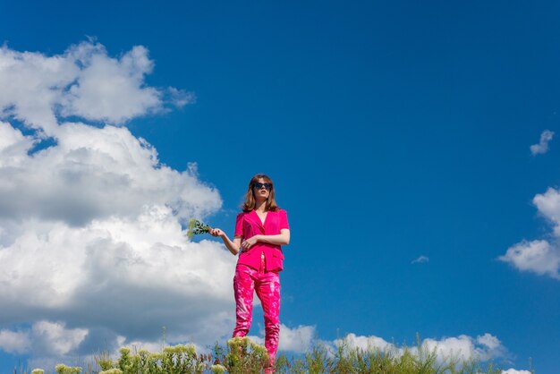 giovane bella ragazza in rosa su uno sfondo di nuvole nel cielo blu estivo.