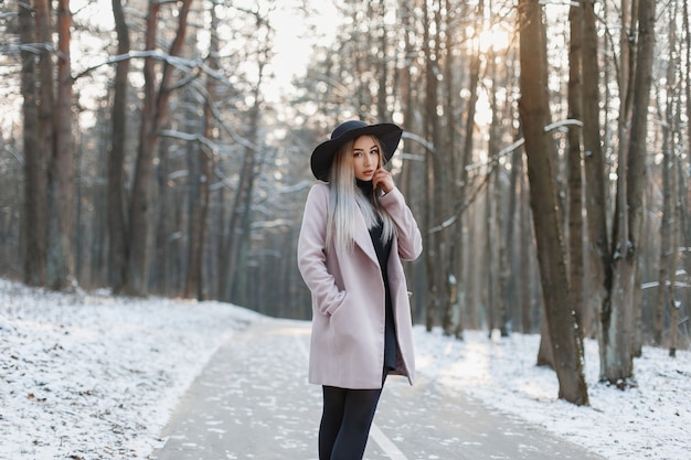 Giovane bella ragazza in un elegante cappello e cappotto che cammina nel parco invernale