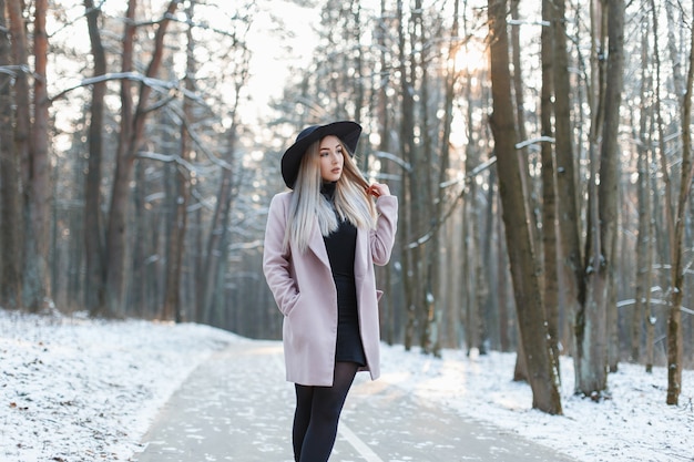 Giovane bella ragazza in un elegante cappello e cappotto che cammina nel parco invernale