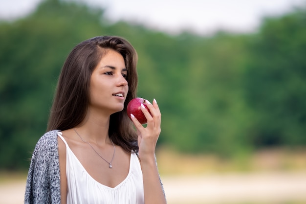 Giovane bella ragazza in vestito bianco che mangia mela organica matura.