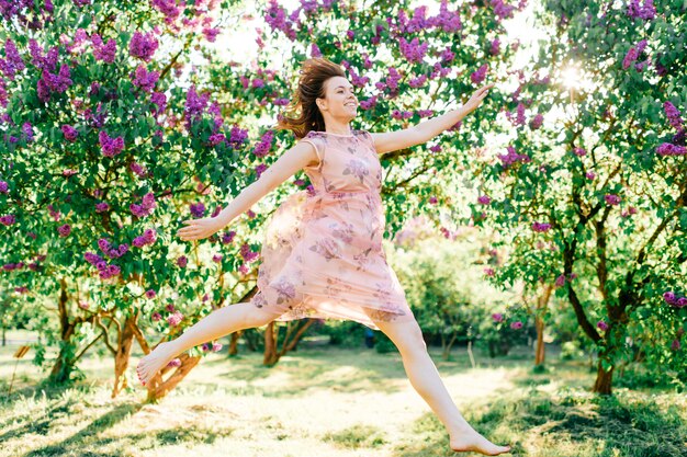 Giovane bella ragazza in vestito rosa che salta nel parco soleggiato