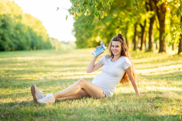 Giovane bella ragazza incinta che si siede sull'erba verde
