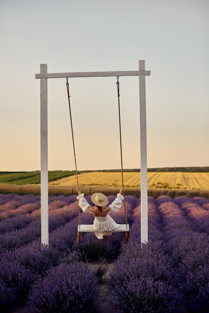 Giovane bella ragazza incinta su un'altalena in un campo di lavanda al tramonto