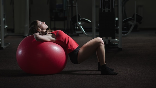 Giovane, bella ragazza sportiva fa esercizi su un fitball in palestra