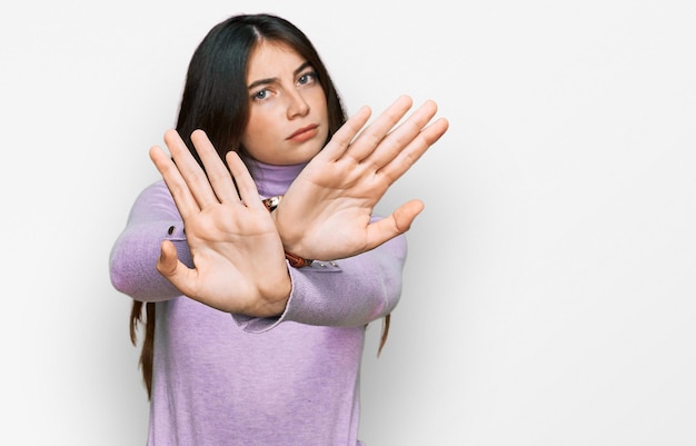 Giovane bella ragazza teenager che indossa maglione a collo alto espressione di rifiuto attraversando le braccia facendo segno negativo, faccia arrabbiata