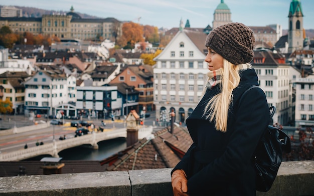 Giovane bella ragazza turistica bionda con cappello caldo e cappotto con zaino che cammina in autunno freddo in Europa città godendo il suo viaggio a Zurigo Svizzera