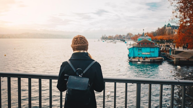 Giovane bella ragazza turistica bionda con cappello caldo e cappotto con zaino che cammina in autunno freddo in Europa città godendo il suo viaggio a Zurigo Svizzera