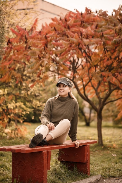 Giovane bella ragazza vestita con abiti eleganti, maglione verde e pantaloni beige, in un parco autunnale con bellissimi alberi