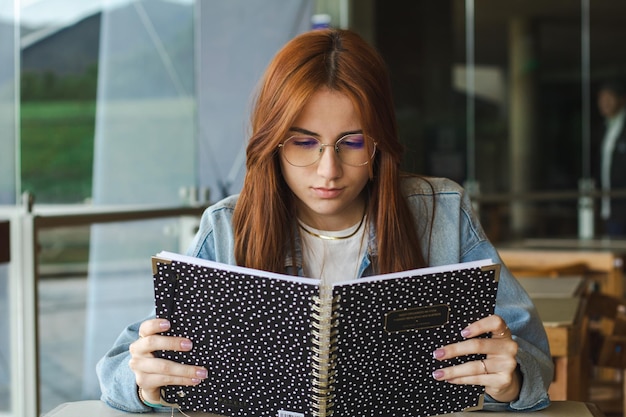 giovane bella studentessa che legge un libro vicino a una finestra in una biblioteca universitaria