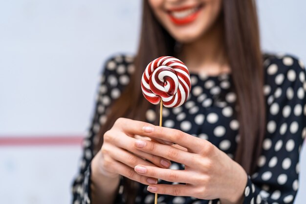 Giovane bellezza in camicia punteggiata con lecca-lecca nelle mani. Signora allegra con caramelle su sfondo bianco.