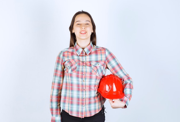 Giovane bello casco di sicurezza della tenuta della donna dell'architetto sopra la parete bianca.