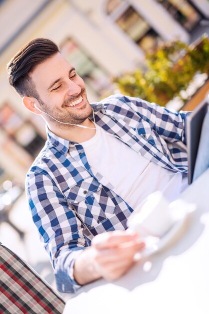 Giovane bello che beve caffè e guarda il suo smartphone